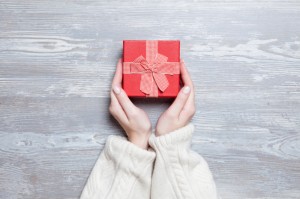 Female hands holding gift on wooden table.